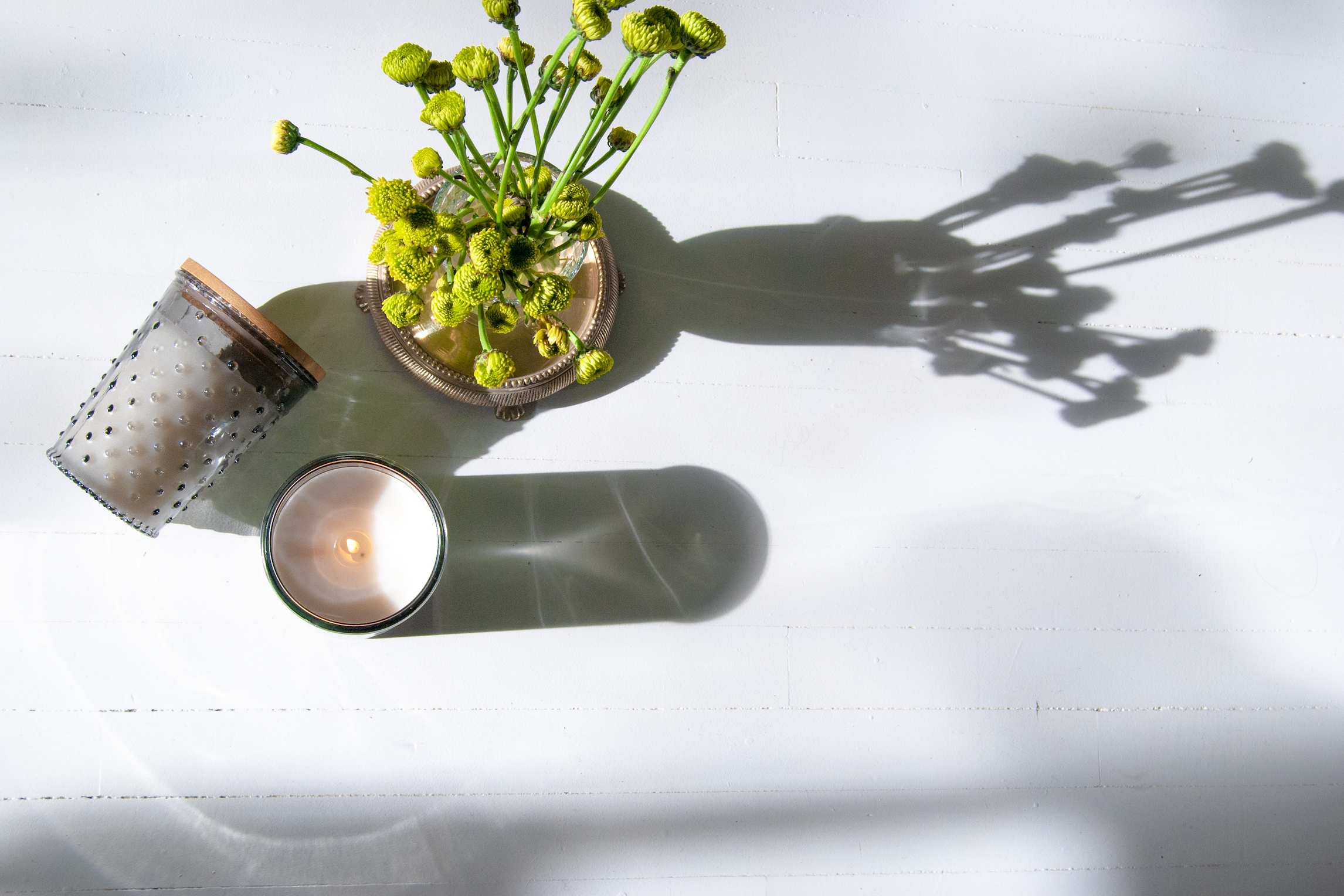Grey hobnail candles on a white floor with small green flowers in a clear vase